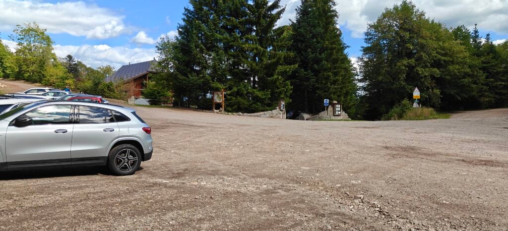 A large gravel area with cars. There are some trees and a rough road in the distance. 